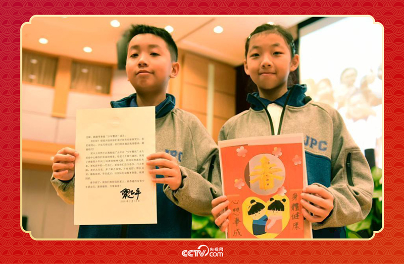 圖為香港“少年警訊”成員郭宏晞（左）展示習(xí)主席回信、羅顥凝（右）展示送給習(xí)主席的賀卡并合影。