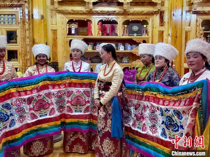 圖為女性展示村民自發(fā)繡制的“百米五彩哈達(dá)”?！±钣穹?攝